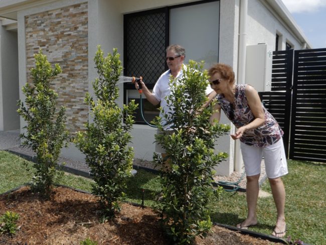 elderly couple watering front garden
